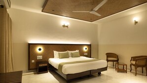 Ein Hotelzimmer mit einem großen Bett, zwei Nachttischen, einem Deckenventilator und einer Sitzecke mit zwei Stühlen und einem kleinen Tisch.