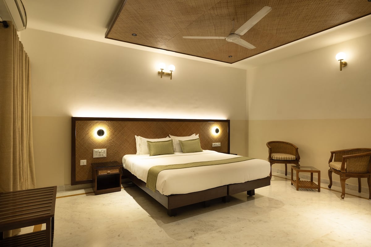 A hotel room with a large bed, two nightstands, a ceiling fan, and a seating area with two chairs and a small table.