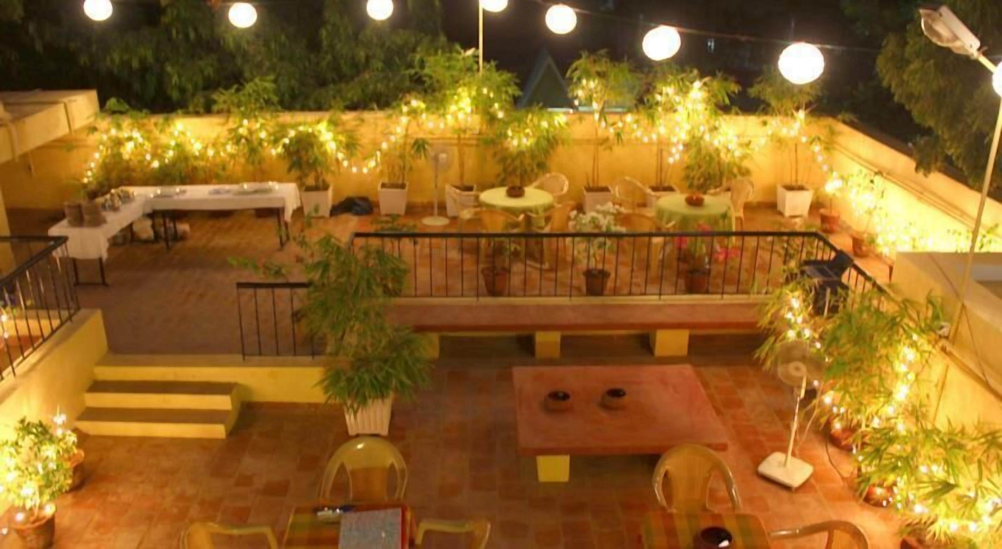 An outdoor patio area with multiple tables and chairs, surrounded by potted plants and string lights.