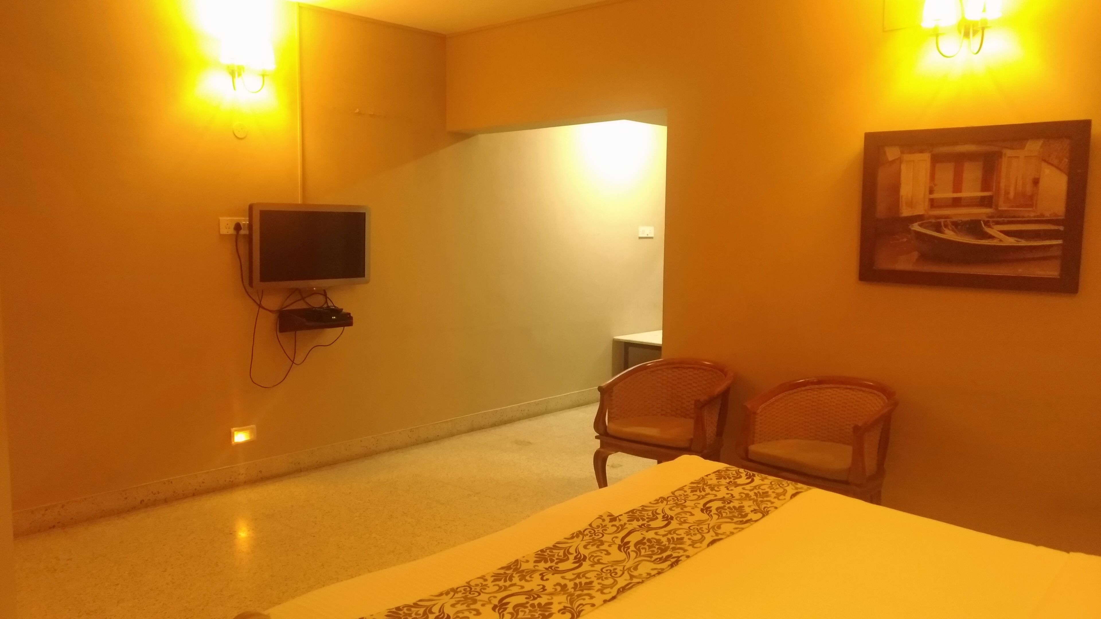 A hotel room with a bed, two chairs, a television, and a painting on the wall.