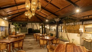 Ein Restaurant mit Holztischen und -stühlen, einer hohen Decke mit hängenden Lampen und einem Fliesenboden.
