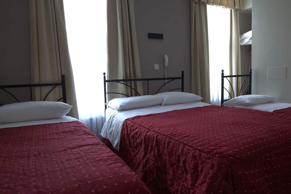 Ein Hotelzimmer mit zwei Einzelbetten, jeweils mit roter Bettdecke und weißen Kissen.