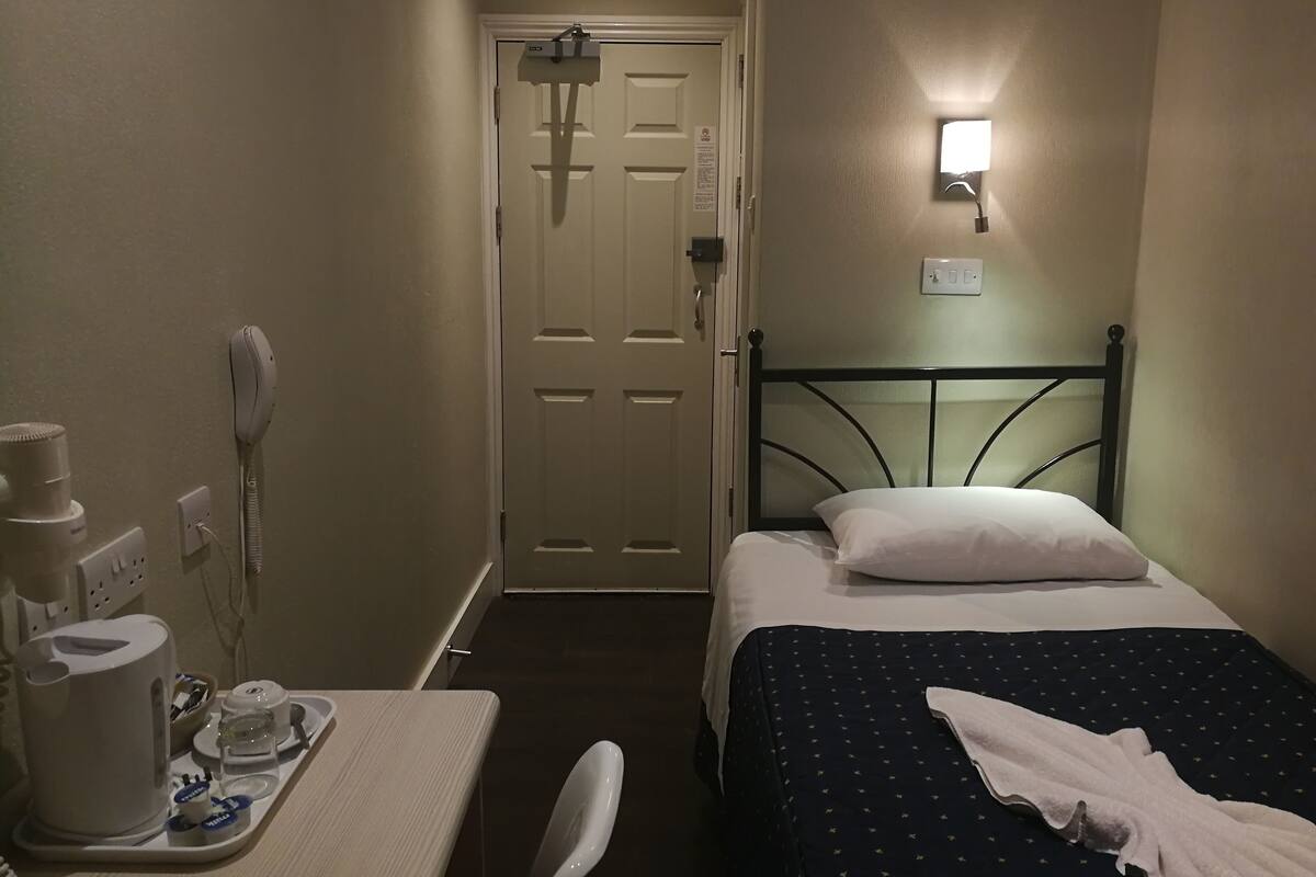 Ein Hotelzimmer mit Bett, Nachttisch und einem kleinen Schreibtisch mit Telefon und Kaffeemaschine.