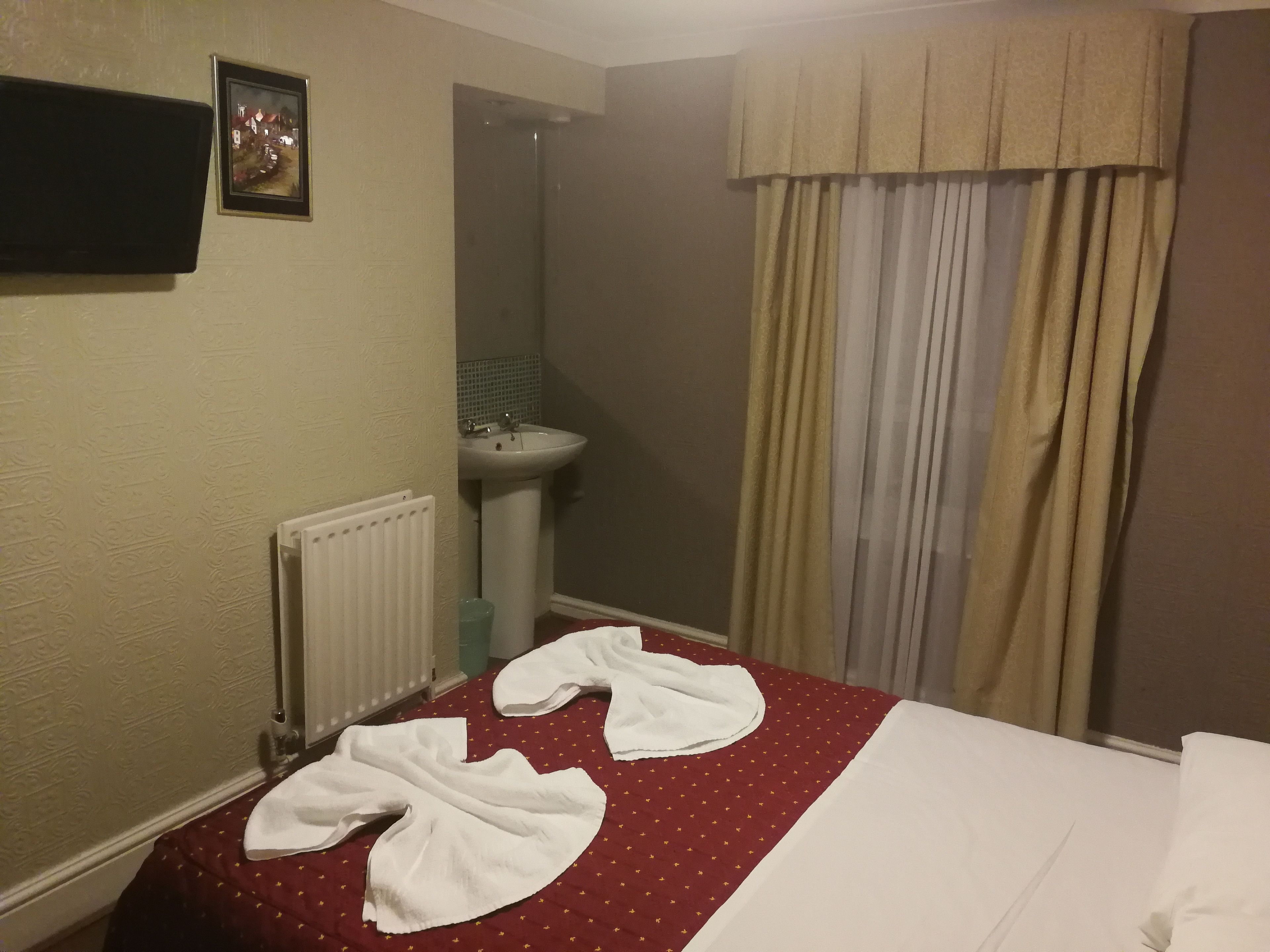 Une chambre d’hôtel avec un lit, un radiateur, un lavabo et une fenêtre avec des rideaux.