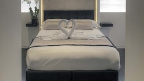 Un dormitorio moderno con una cama grande, cabecera con iluminación integrada, mesita de noche con una planta y ventana con vistas.