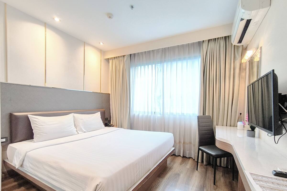 A hotel room with a large bed, a desk with a chair, a television, and a window with curtains.
