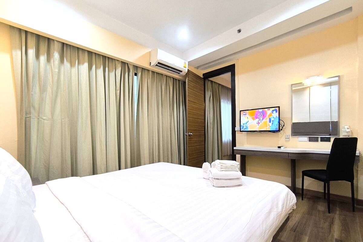 A hotel room with a bed, a desk with a chair, a television, and a mirror.