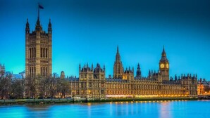 A historic building complex with multiple towers and a prominent clock tower, likely a government or parliamentary building, by a river. - Apollo Hotel Kings Cross (London)