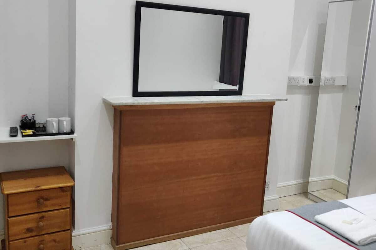 Une petite pièce propre, avec une commode en bois, un lit et un miroir au mur.