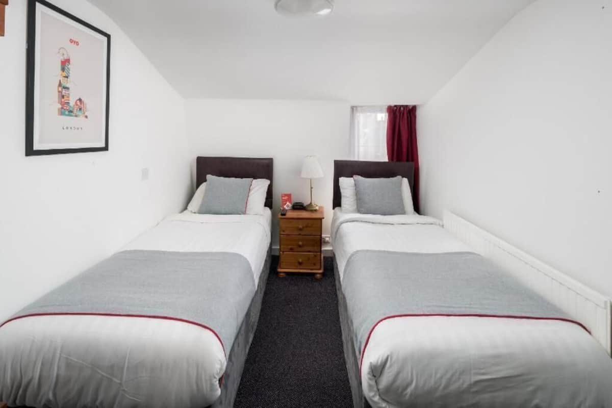 Une chambre double avec deux lits, une table de chevet, une lampe et un tableau encadré au mur.
