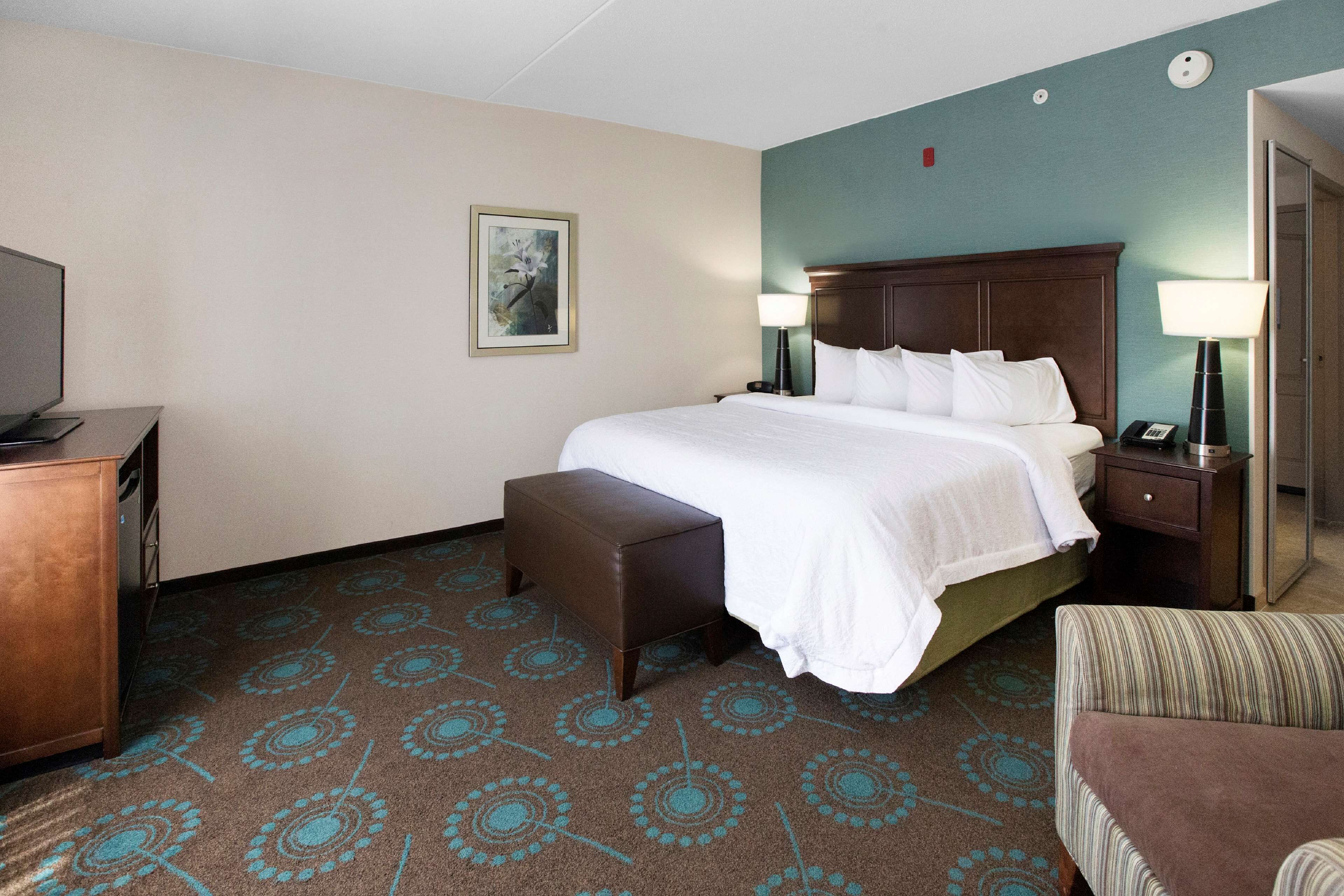 A hotel room with a bed, a bench, a TV, and a desk.