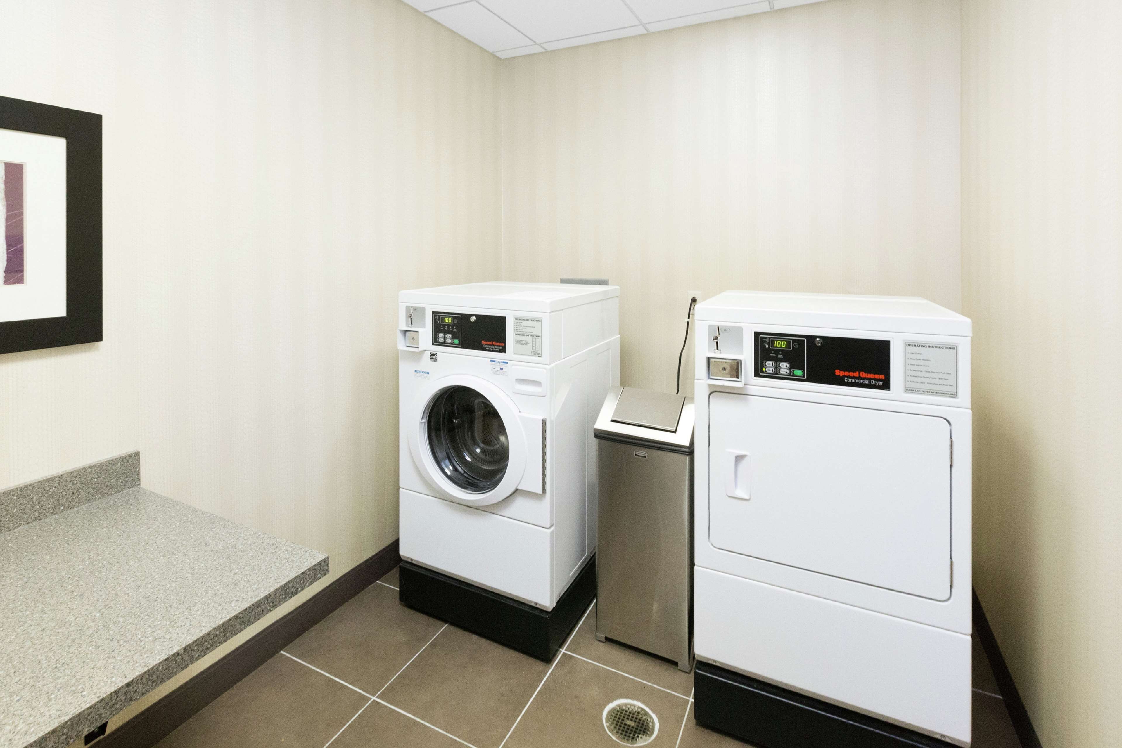 A laundry room with two washing machines and a small trash bin.