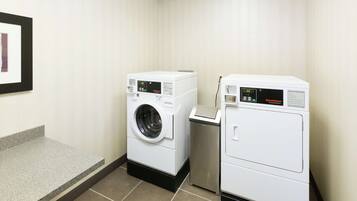 A laundry room with two washing machines and a small trash bin.