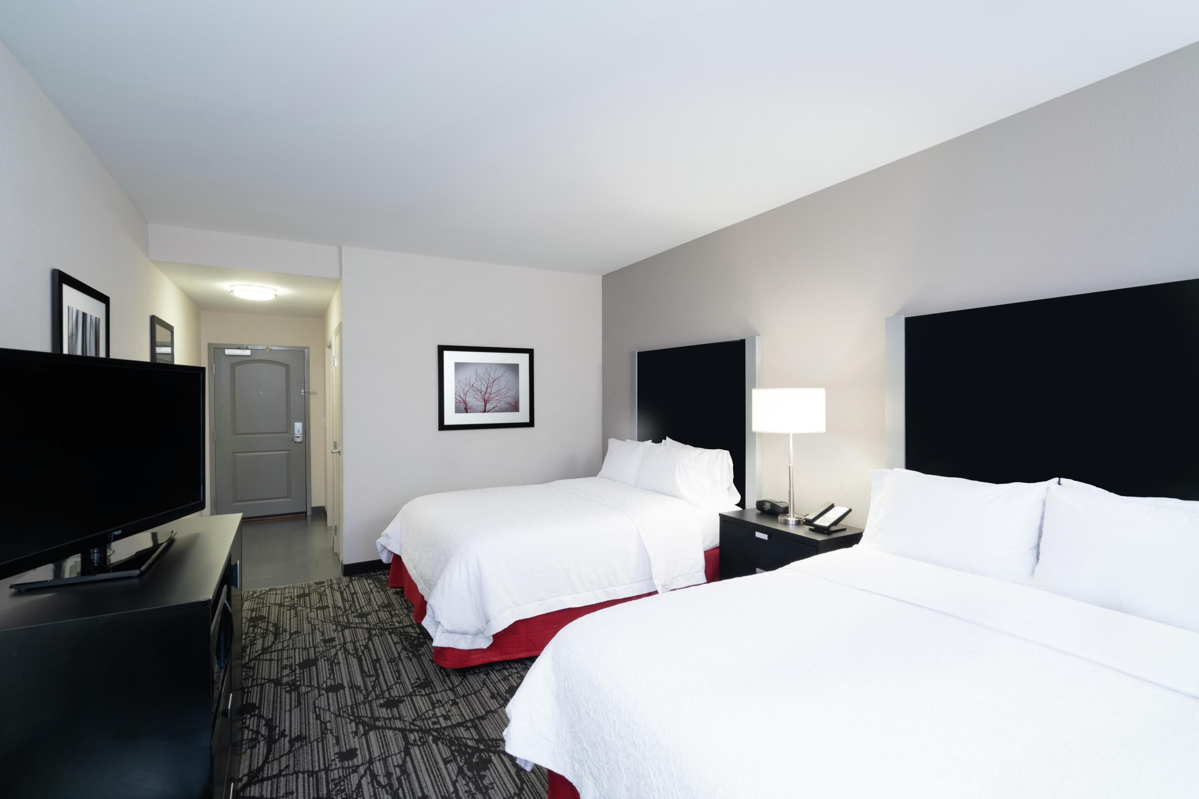 A hotel room with two beds, a flat-screen TV, a desk, and a framed picture on the wall.