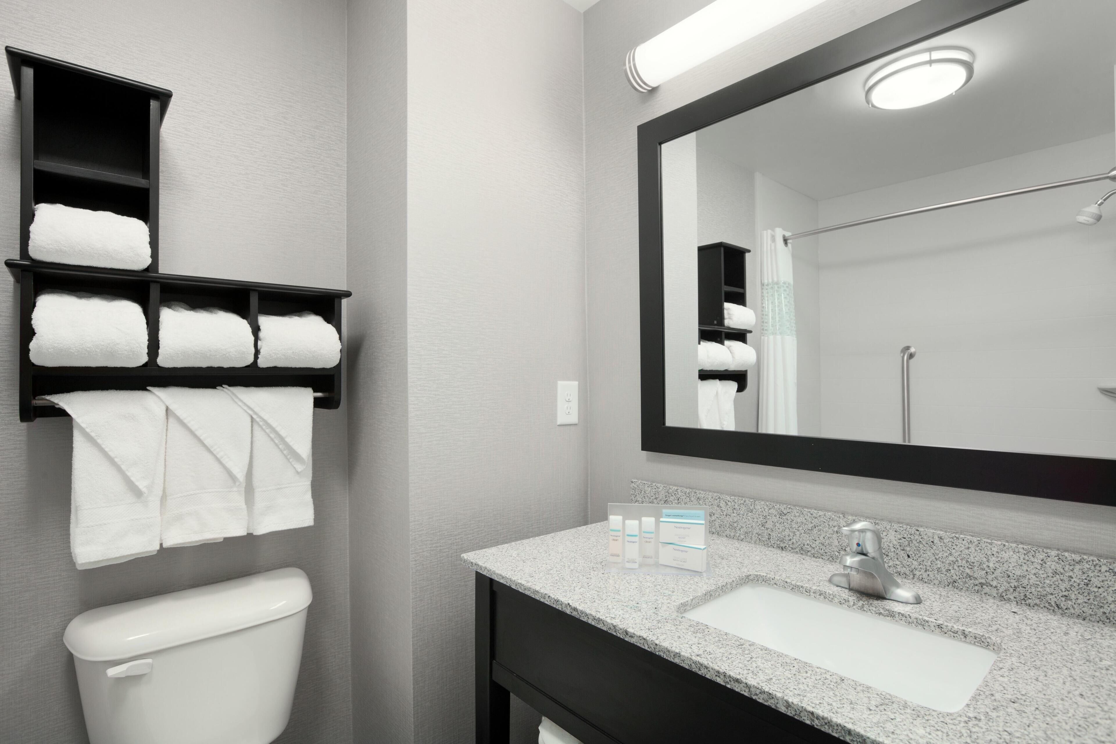 A bathroom with a toilet, a sink with a mirror, and shelves with towels.