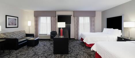 Una habitación de hotel con un sofá, dos camas, un escritorio, una silla y un televisor.