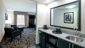 A hotel room with a kitchenette, a large mirror, a seating area with a chair and a small table, and a carpeted floor. - Hampton Inn & Suites Roanoke Airport (Roanoke)