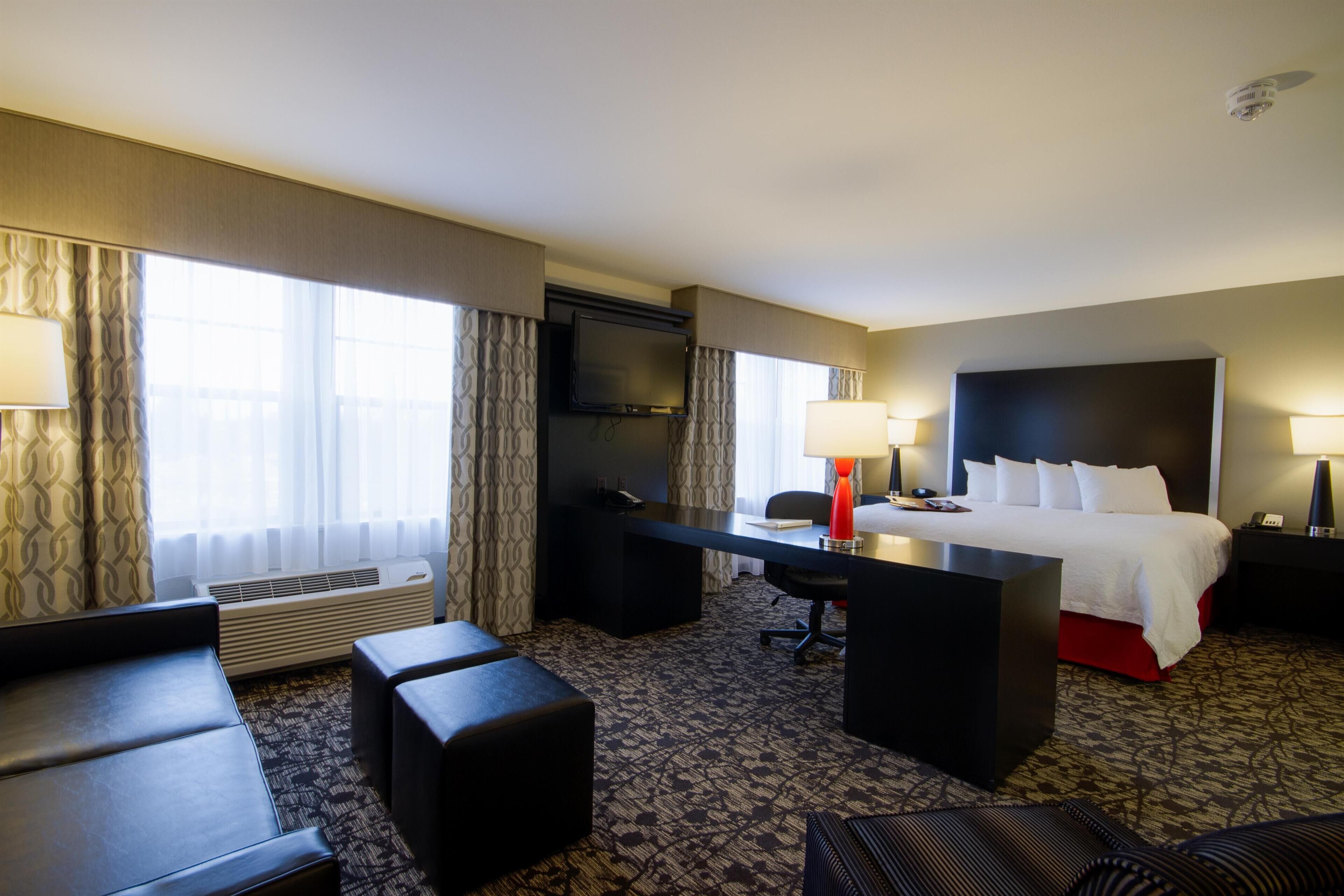 Ein Hotelzimmer mit Bett, Schreibtisch, zwei Stühlen, Fernseher und einem Fenster mit Vorhängen.