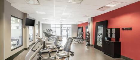 Un gimnasio con cintas de correr, pesas y una pared roja.