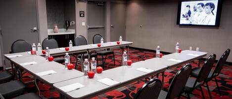 A conference room with a long table, chairs, water bottles, apples, and a TV screen.