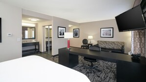 A hotel room with a bed, a desk, a sofa, a TV, a lamp, and framed pictures on the wall. - Hampton Inn & Suites Roanoke Airport (Roanoke)