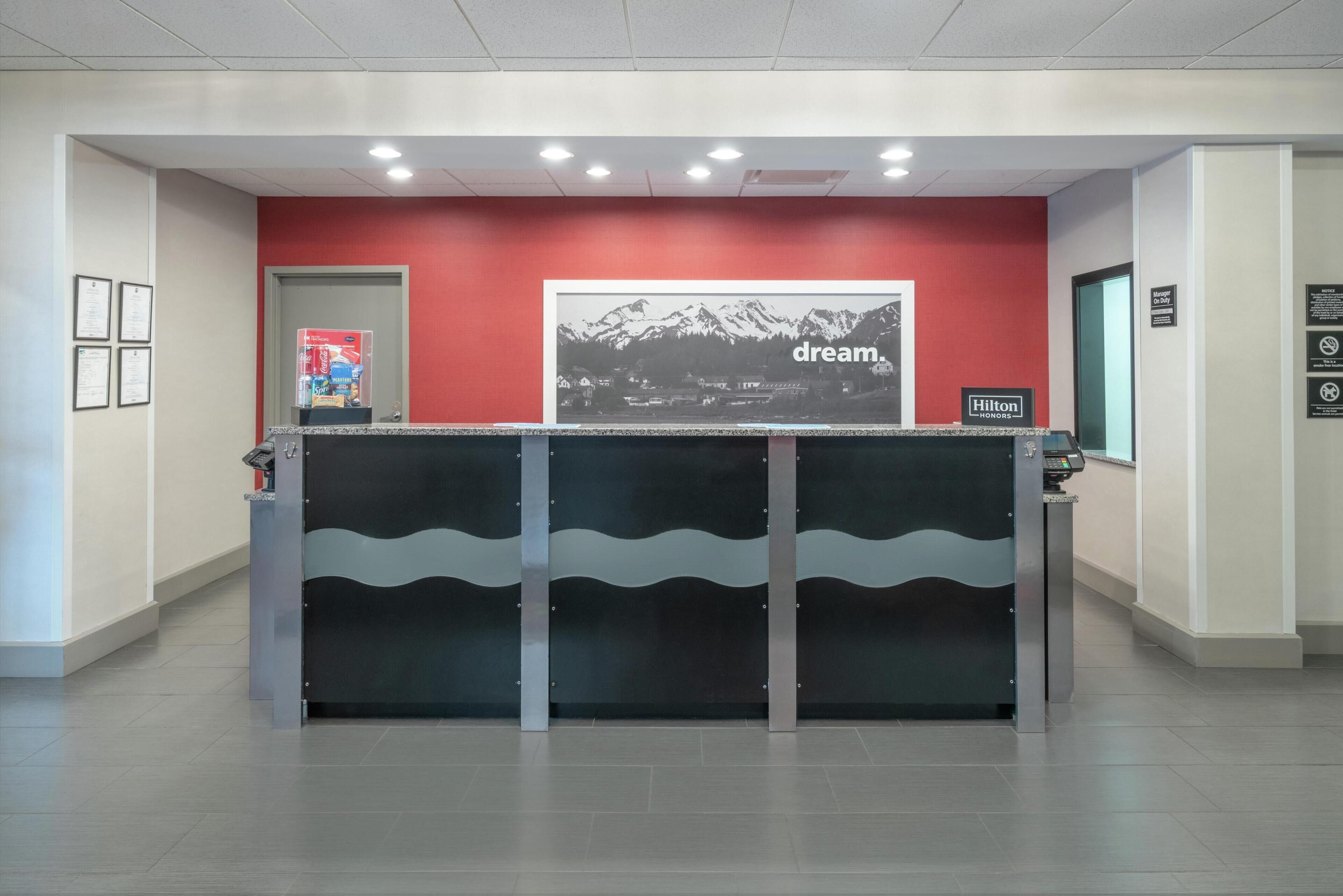 A hotel reception desk with a red wall, a framed picture of mountains, and a 'dream' sign.