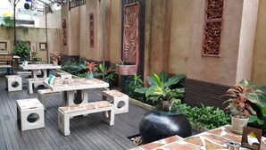 An outdoor patio area with multiple tables and benches, surrounded by potted plants and decorative wall panels. - Best Beach Villa (Pattaya)