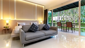 A modern hotel room with a sofa, a bedside table, and a view of a garden through large windows. - The Palmery Resort (Karon)