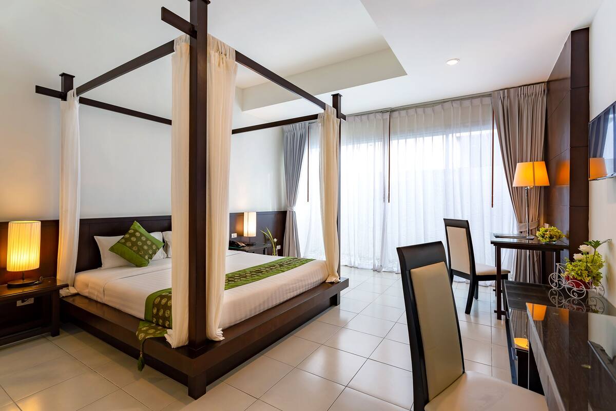 A four-poster canopy bed with a nightstand, a desk with a chair, and a TV on the wall.