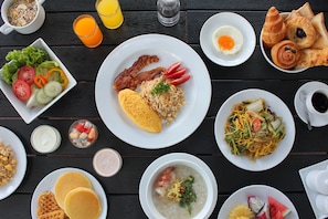 Variedad de platos para el desayuno, como huevos, tocino, tortitas y un plato de fideos, sobre una mesa de madera.