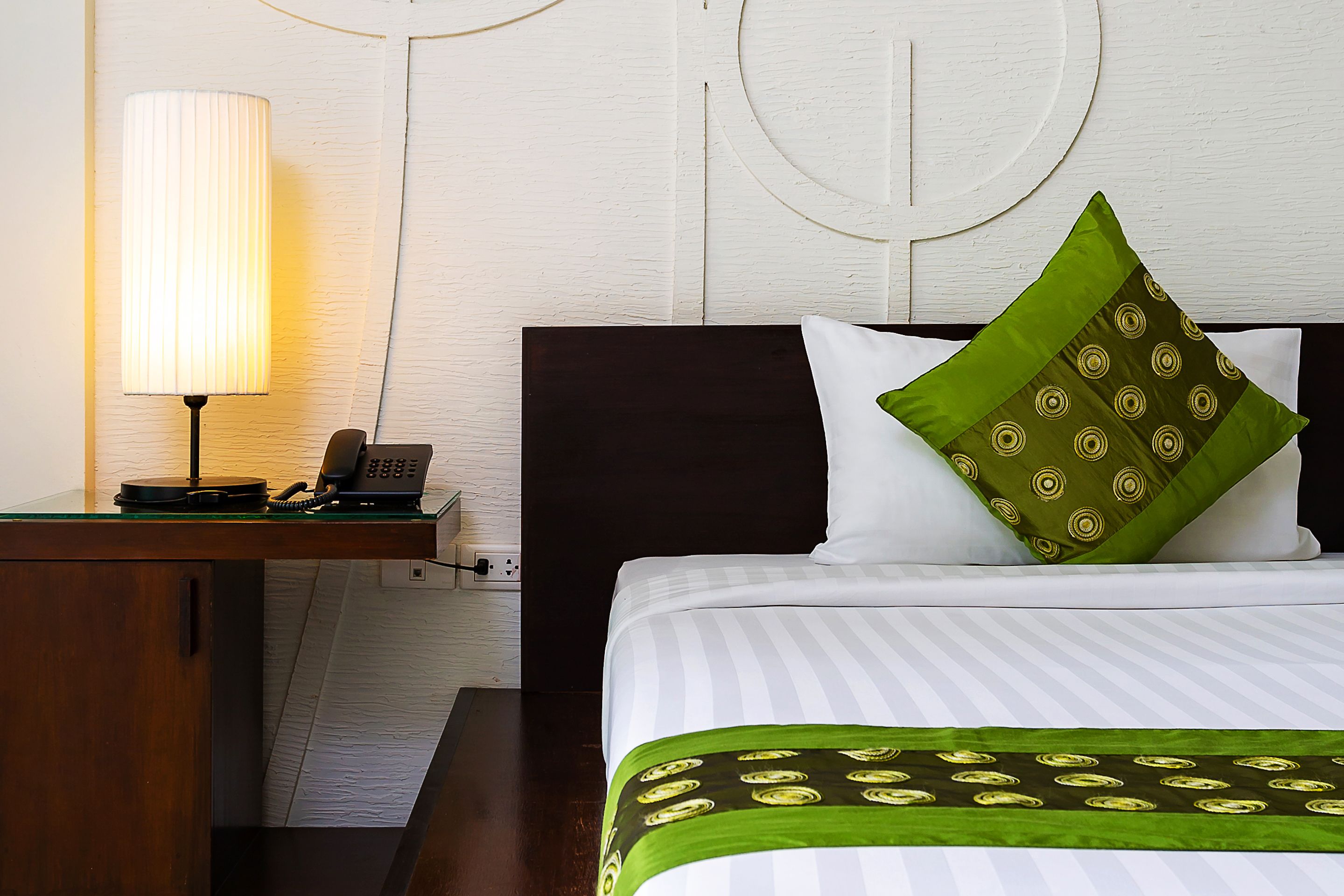 A hotel room with a bed, a nightstand with a lamp, and a telephone.