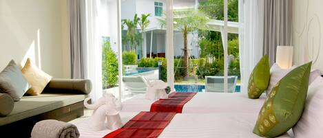 A hotel room with a large bed, a sofa, and a view of a swimming pool and greenery.