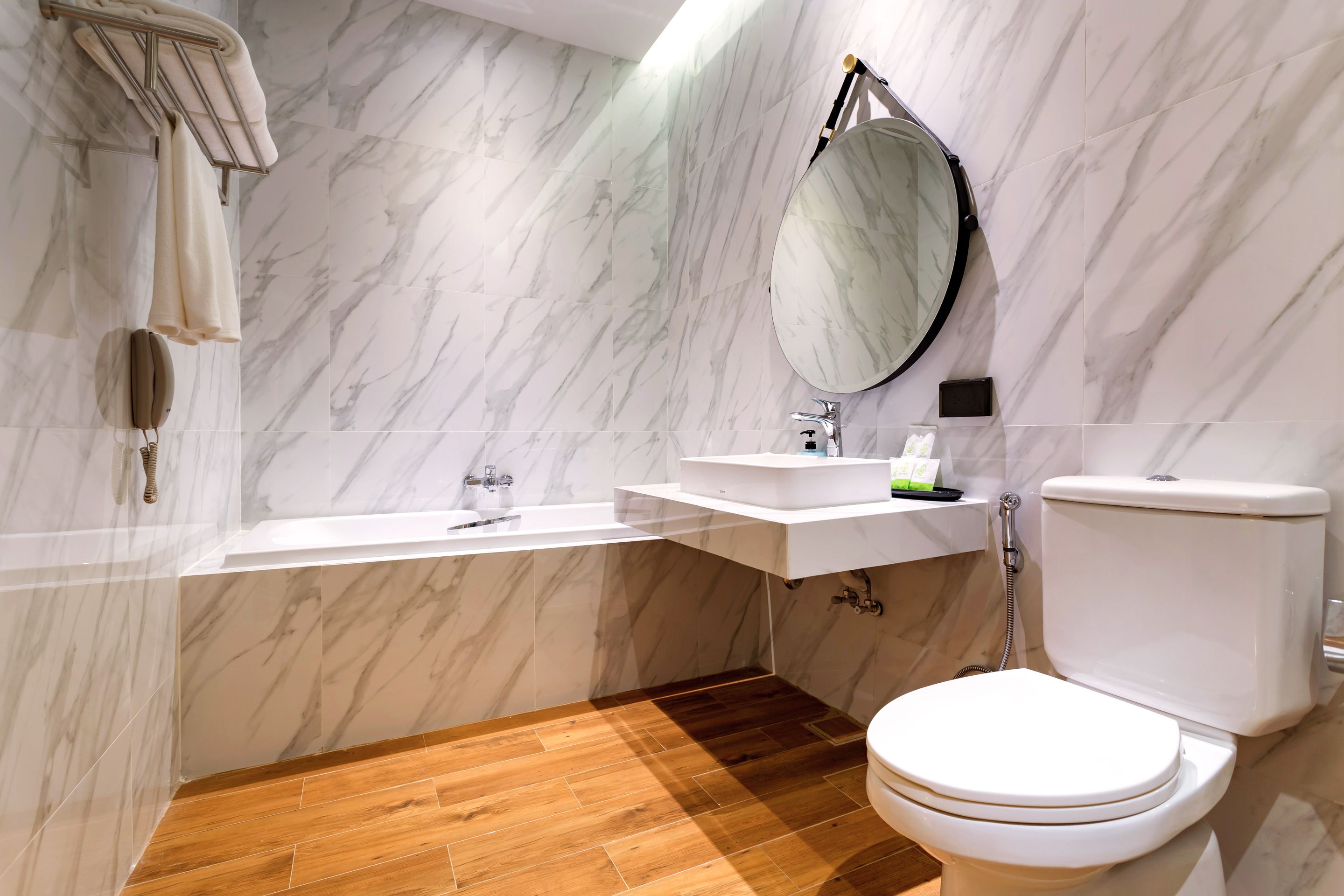 A bathroom with a marble wall, a wooden floor, a white toilet, a sink, and a bathtub.
