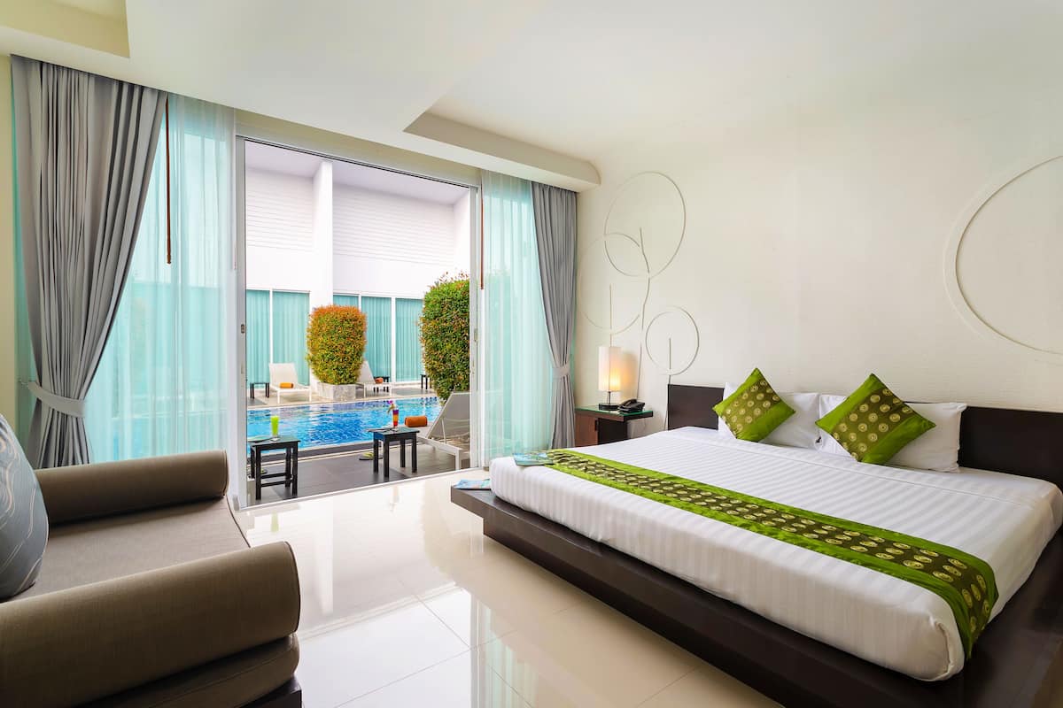A hotel room with a large bed, a sofa, a small table, and a view of an outdoor swimming pool.