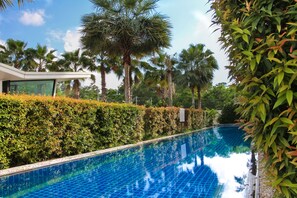 Una piscina con borde de azulejos, rodeada de exuberante vegetación y palmeras.