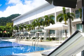 A pool area with lounge chairs and umbrellas, a modern building with balconies, and a mountain backdrop. - The Palmery Resort (Karon)