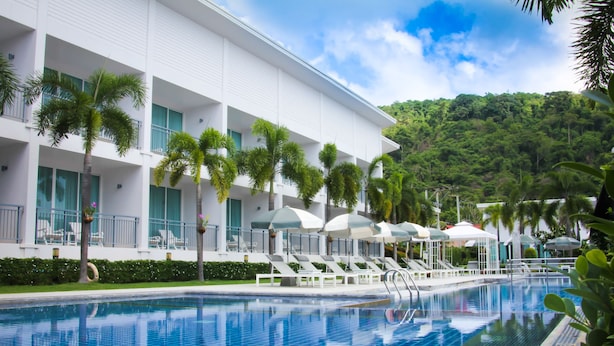 A hotel with a swimming pool, palm trees, and a view of a lush green hill. - The Palmery Resort (Karon)