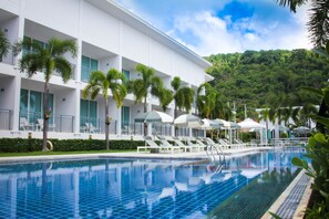 A hotel with a swimming pool, palm trees, and a view of a lush green hill. - The Palmery Resort (Karon)