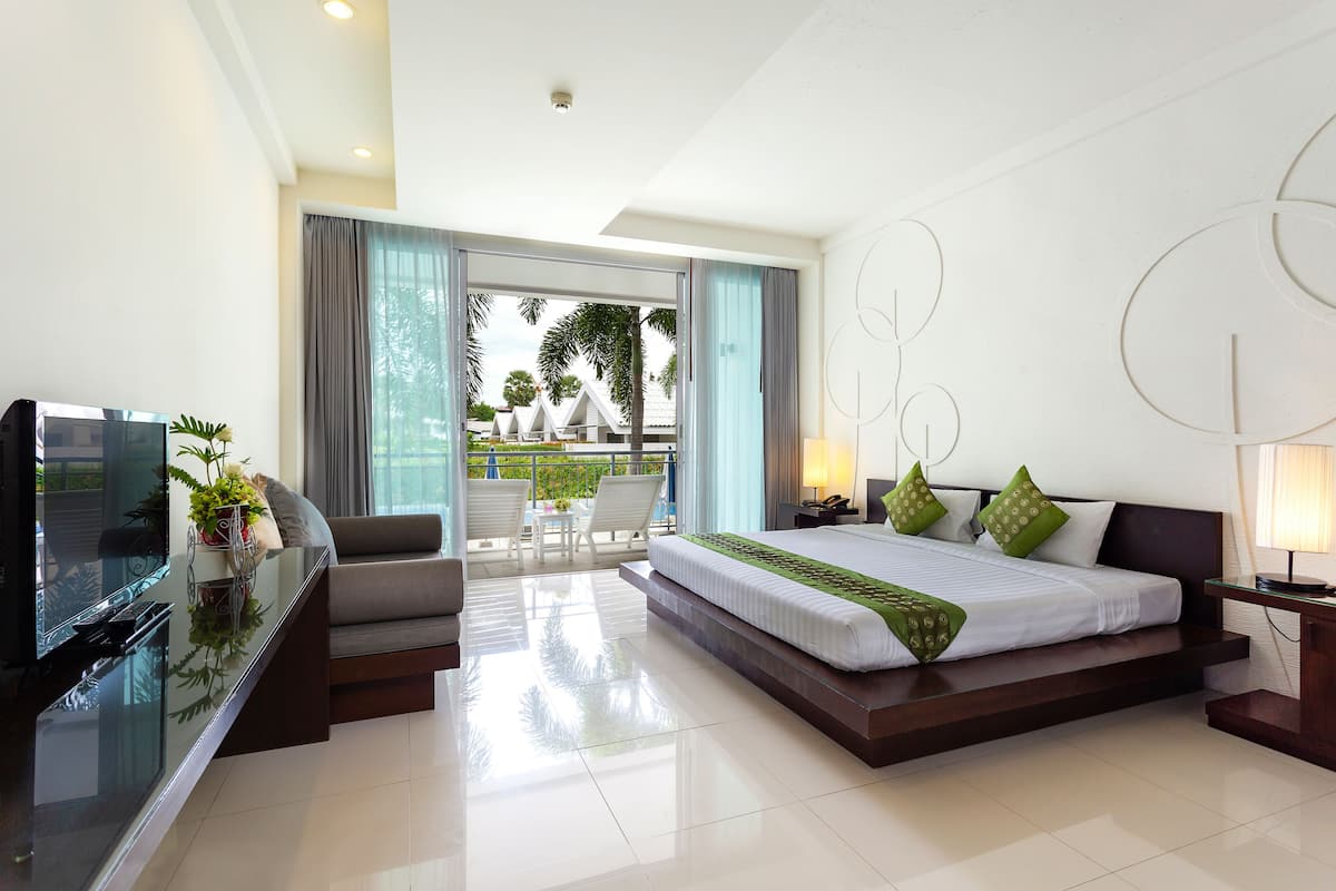 A modern hotel room with a large bed, a TV, a sofa, and a balcony with a view of palm trees.