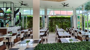 A spacious indoor dining area with multiple tables and chairs, large windows, and ceiling fans. - The Palmery Resort (Karon)
