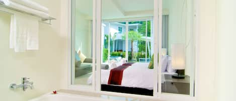 A modern bathroom with a large bathtub, a glass shower enclosure, and a view of a bedroom with a bed and a balcony.