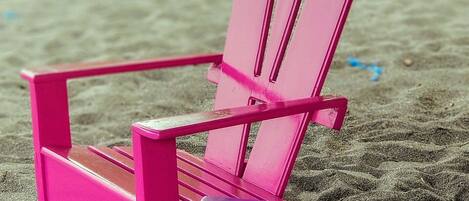 Escena de playa con dos sillas de playa, una rosa y otra morada, sobre la arena.