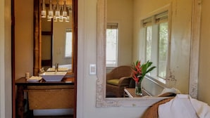 A bathroom with a sink, mirror, and a chair near the window.