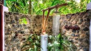 A stone wall with a water spout and a bamboo pipe, surrounded by greenery.