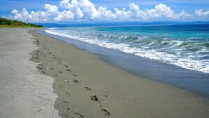 A beach with footprints leading into the ocean, a clear sky, and distant mountains.