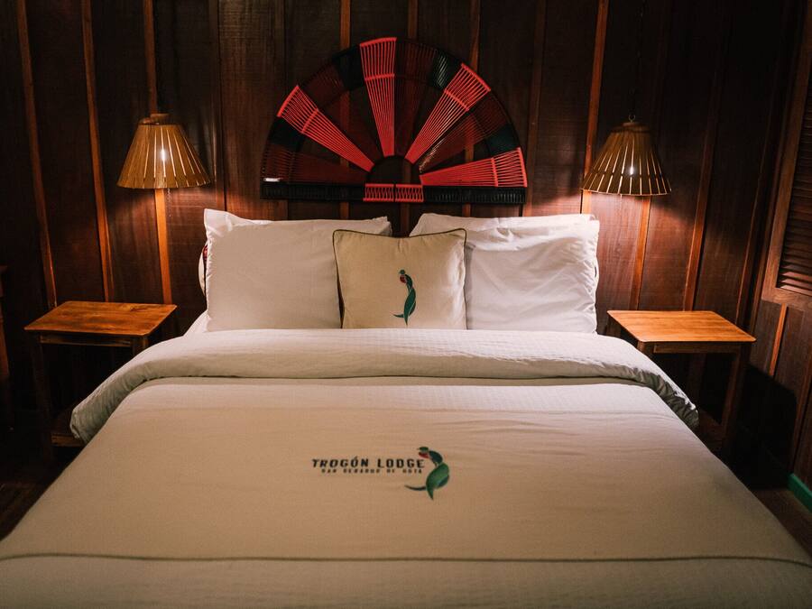 A hotel room with a bed, two nightstands, a decorative fan, and a lamp on each nightstand.