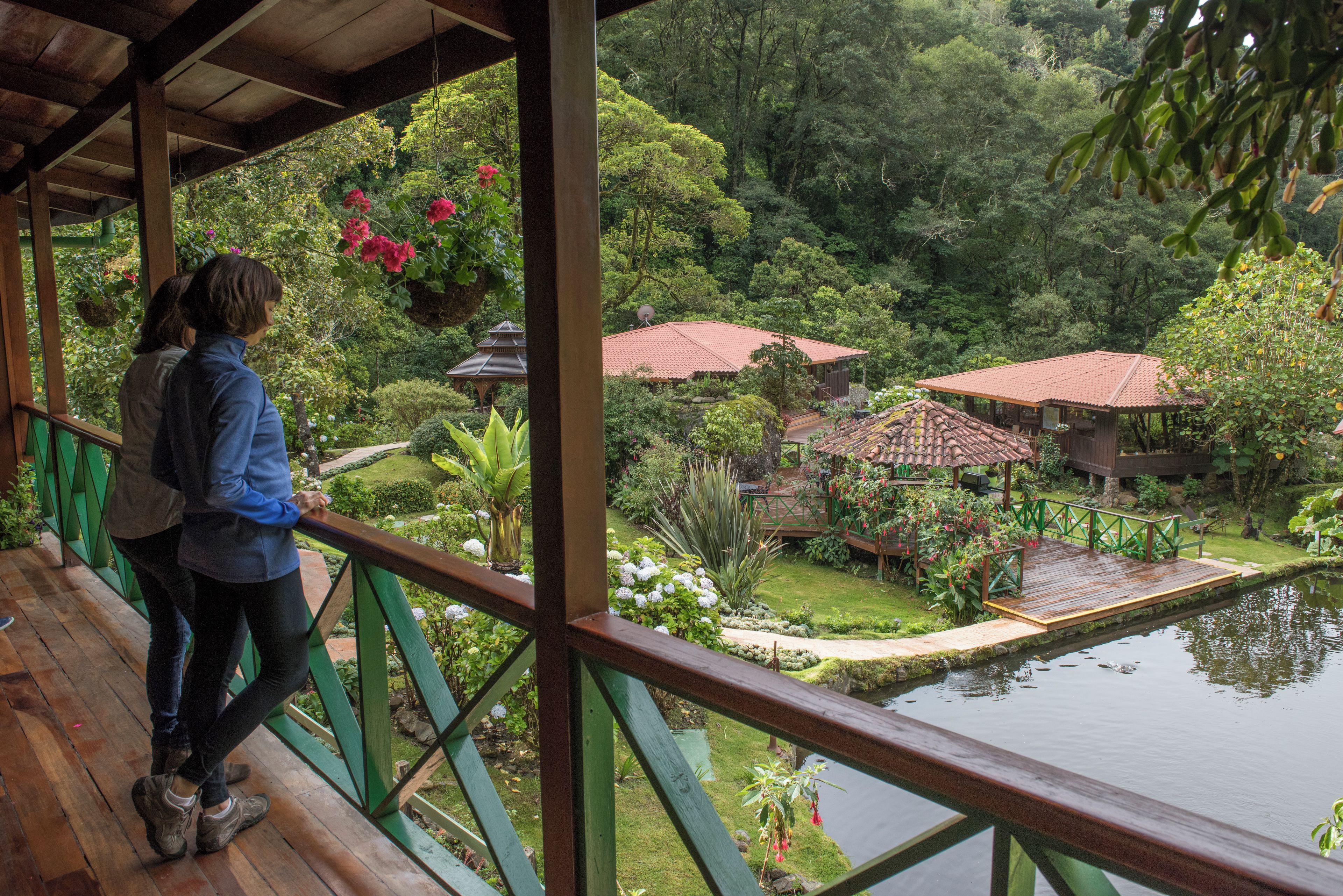 Una terraza de madera con vistas a un jardín que incluye un estanque y edificios de estilo tradicional.