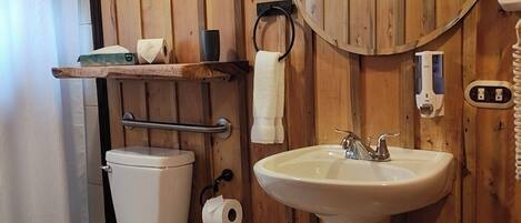 A wooden-paneled bathroom with a toilet, sink, and a window above the toilet.