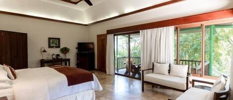 A spacious bedroom with a large bed, a ceiling fan, and a balcony with a view of greenery.