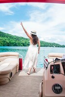 Mulher de vestido branco está no convés de um barco, apontando para a água.